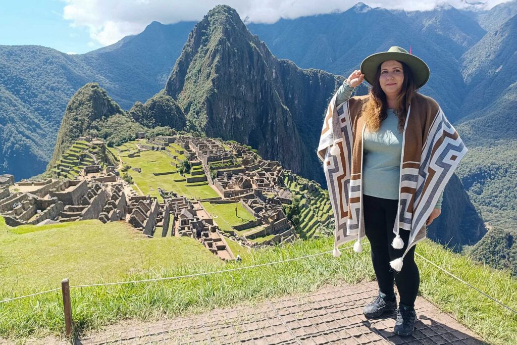 Tourist posing in front of the ancient Inca citadel of Machu Picchu, surrounded by green mountains in Cusco, Peru.